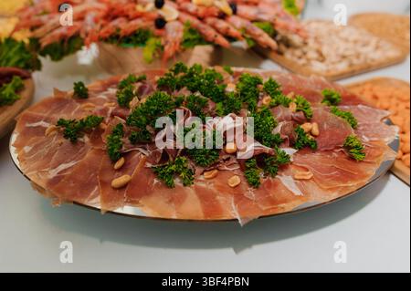 Un gros plan saisissant présente un plateau de charcuterie abondant avec de délicates tranches de prosciutto garnies de persil et de pignons de pin Banque D'Images