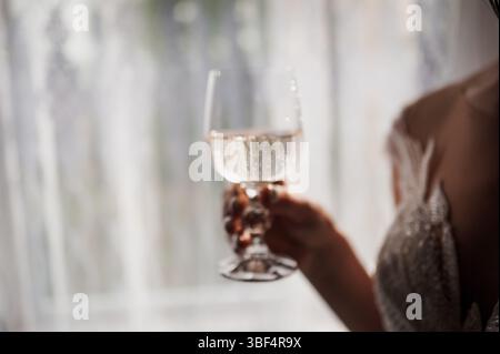 Une vue rapprochée floue capture une femme vêtue d'une robe scintillante tenant une flûte à champagne remplie de vin ros, faisant allusion à un mariage ou à une célébration haut de gamme Banque D'Images