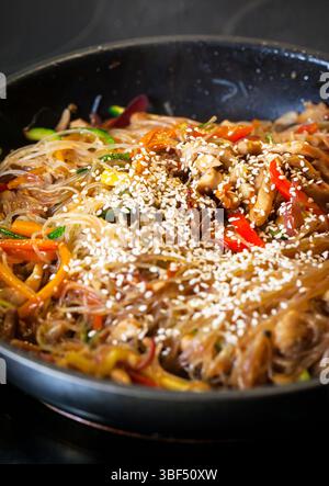 Nouilles asiatiques en verre sauter avec du poulet et des légumes dans une poêle Banque D'Images
