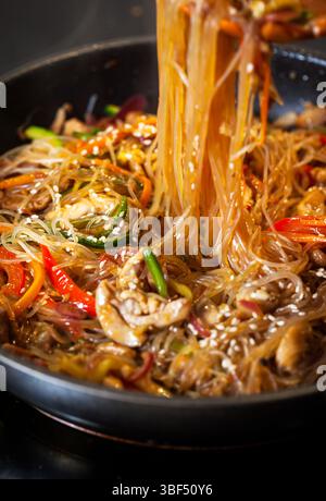 Nouilles asiatiques en verre sauter avec du poulet et des légumes dans une poêle Banque D'Images