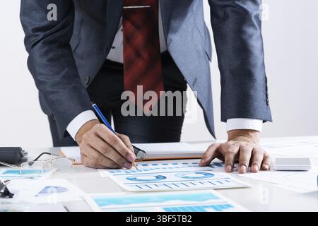 Homme d'affaires debout près du bureau et analysant les graphiques financiers. Directeur d'entreprise réussi en costume d'affaires et cravate. Gros plan main homme avec pe Banque D'Images