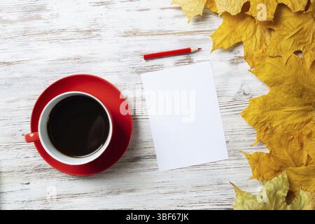 Composition d'automne plate avec tasse de thé noir et feuilles d'automne jaunes. Concept Time of tea break. Boisson chaude et feuille de papier vierge avec stylo se trouve o Banque D'Images
