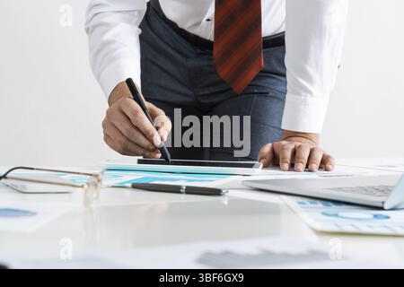 Homme d'affaires se tenant près du bureau et analysant les diagrammes financiers. Directeur d'entreprise réussi en costume et cravate d'affaires. Gros plan main homme avec un Banque D'Images