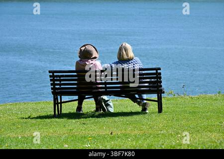Deux dames prenant un repos au soleil, sur un banc en métal noir UK May Banque D'Images