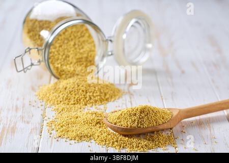 Grains jaunes de millet bio dans une pelle en bois et dans un pot de stockage en verre sur une table lumineuse, mise au point sélective. Banque D'Images