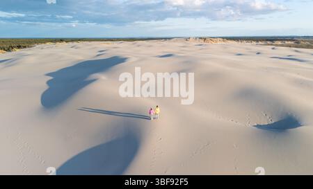 Deux individus se promènent dans le vaste paysage sablonneux du Danemark, entouré de dunes ondulantes sous un magnifique ciel de coucher de soleil. Rabjerg Mile Dunes, Danemark. Banque D'Images
