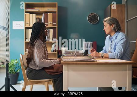 Consultation femme caucasienne d'âge moyen aidant jeune femme noire adulte Banque D'Images