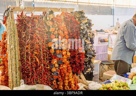 Légumes séchés colorés suspendus au marché local avec des acheteurs occupés en arrière-plan. Banque D'Images