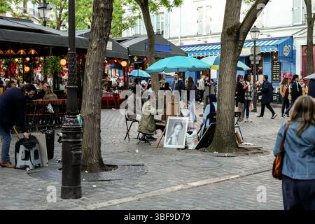Scène de rue animée dans une ville européenne, probablement Paris, avec des artistes dessinant des portraits sous des parapluies colorés et des personnes profitant d'un café en plein air Banque D'Images