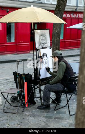 Un artiste de rue, vêtu d'un masque et assis sous un grand parapluie, dessine un portrait sur un chevalet place du Tertre, Montmartre, Paris, avec un buil rouge Banque D'Images