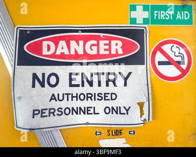 Photographie d'un panneau d'interdiction d'entrée et de fumée vieux, sale et endommagé situé sur une porte coulissante jaune dans un bâtiment industriel. Banque D'Images