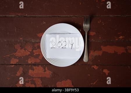 2024 écrit sur un morceau de papier dans une assiette avec fourchette sur la surface en bois rouge, plan d'affaires, objectifs, temps et délais Banque D'Images