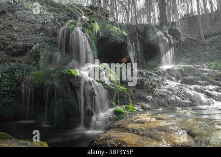 De douces cascades coulent sur des formations rocheuses moussues dans une forêt isolée. La longue exposition révèle une eau fluide, tandis que les textures de la pierre Banque D'Images