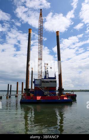 Kiel, Allemagne - 28. Mai 2025 : grue et barge d'empilement travaillant sur le front de mer de Kiel sous ciel nuageux en Allemagne Banque D'Images