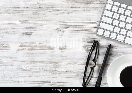 Nature morte de l'espace de travail de bureau avec tasse de café et fournitures. Bureau plat en bois blanc avec clavier d'ordinateur, lunettes et stylo. Heure de la pause café. Banque D'Images