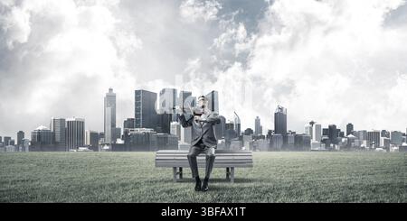 Jeune homme portant costume et lunettes assis sur un banc et à jouer du violon Banque D'Images