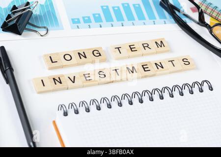 Concept d'investissements à long terme avec des lettres sur des cubes en bois. La vie de bureau reste encore en stock. Surface blanche à poser à plat avec bloc-notes, stylo et Banque D'Images