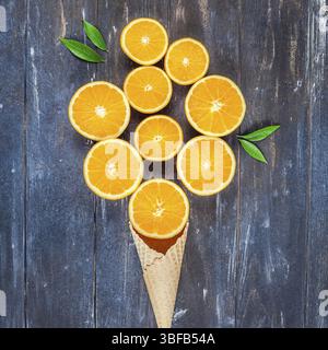 Plat à l'obscurité créative jeter Vue de dessus des tranches de fruits d'orange dans la crème glacée cornet gaufré sur fond de table en bois brun avec copie espace. Un minimum de Banque D'Images