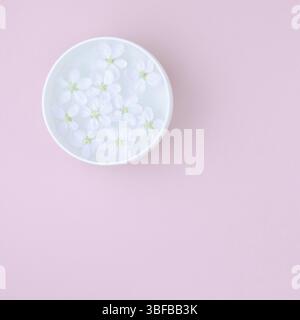 Télévision créative concept laïcs vue du dessus de l'aroma bol avec de l'eau et de blanc de printemps fleurs de pommier en fleurs rose pastel sur fond carré de papier avec Banque D'Images