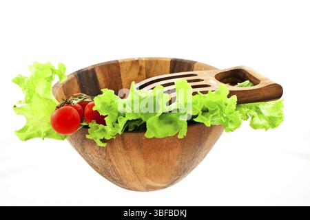 Feuilles de laitue verte et bouquet de tomates dans un saladier en bois avec une grande fourchette en bois sur fond blanc Banque D'Images