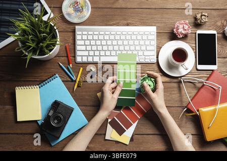 Concepteur Web choisissant des couleurs à partir de nuances au bureau en bois. Bureau vue de dessus avec clavier d'ordinateur et papeterie. Conception de l'interface utilisateur o Banque D'Images