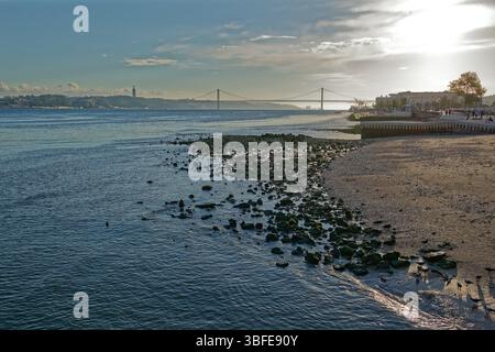 Une photographie aérienne représente une vue du Tage à Lisbonne, au Portugal. Le premier plan montre une plage de sable noir avec de nombreux petits rochers et galets Banque D'Images
