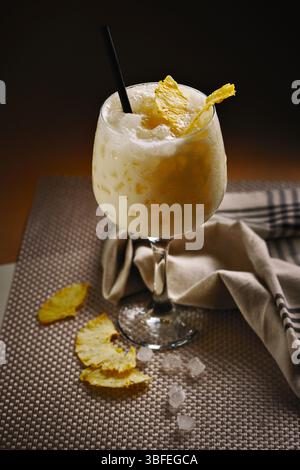 Gros plan du cocktail Pina Colada servi dans un verre avec de la glace pilée, une garniture d'ananas séché et de la paille noire. Banque D'Images