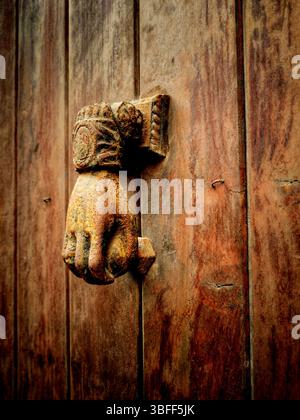 Un frappeur de porte vintage en forme de main est monté sur une porte en bois vieilli, présentant des conceptions complexes et une patine riche Banque D'Images