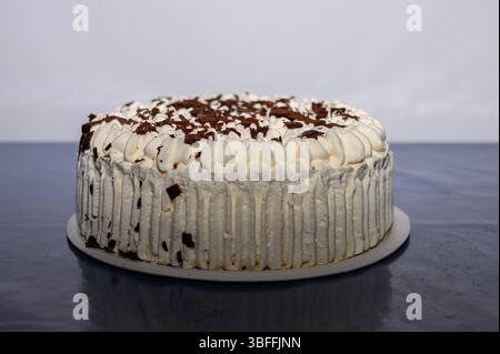 Un gâteau à la crème superposée joliment décoré se trouve sur une table avec de riches copeaux de chocolat sur le dessus. Le gâteau présente un glaçage blanc lisse et un invit Banque D'Images