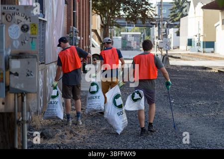 Portland, Oregon - 17 août 2017 : des volontaires de SOLVE nettoyent les ordures le long d'une rue. Ils portent des gilets orange et transportent des sacs poubelles. Banque D'Images