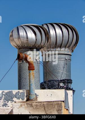 Paire de ventilateurs à turbine tournant sur le toit du bâtiment, améliorant la ventilation contre le ciel bleu clair Banque D'Images