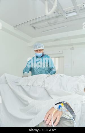 Un médecin dans une salle d'opération effectue une intervention chirurgicale sur un patient relié à un IV, entouré d'un équipement médical. Banque D'Images