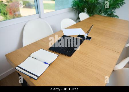 Un espace de travail élégant comprenant un ordinateur portable, un ordinateur portable et un smartphone sur une table en bois dans un bureau à domicile éclairé par la lumière du soleil. Idéal pour la productivité, à distance Banque D'Images