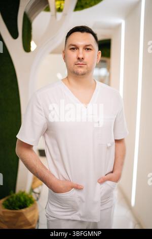 Masseur masculin confiant debout avec les mains dans les poches dans le centre de spa moderne, mettant en valeur le professionnalisme et l'expertise dans le bien-être et les soins du corps. Banque D'Images