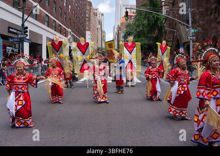Un défilé de rue avec de multiples danseurs dans des costumes rouges et dorés vifs, ornés de coiffes. Ils portent de grandes bannières décorées et défilé Banque D'Images