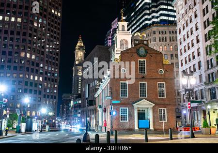 Vue nocturne de l'historique Old State House à Boston, Massachusetts, entouré de gratte-ciel modernes et de lampadaires légèrement éclairés. Le bâtiment de l'époque coloniale se distingue par sa façade en briques rouges et son balcon emblématique, marquant un site important dans l'histoire américaine Banque D'Images