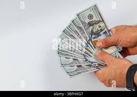 Deux mains trient à travers un éventail de billets de cent dollars, mettant en valeur la manipulation méticuleuse de l'argent liquide dans un cadre neutre. Banque D'Images