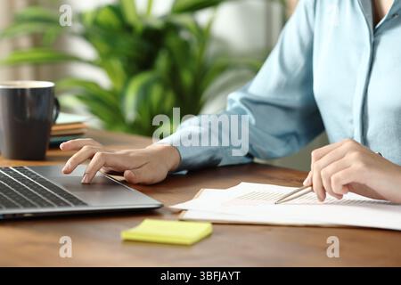 Gros plan d'une main de femme travaillant comparant le document avec le contenu en ligne au bureau Banque D'Images