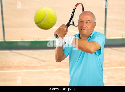 portrait d'un ancien joueur de tennis debout et frappant la balle sur un court de terre battue Banque D'Images