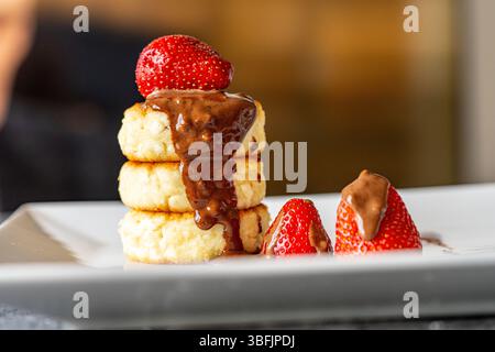 Crêpes au fromage cottage ou gâteaux au fromage avec fraises et chocolat sur une assiette blanche. Le concept d'un petit déjeuner délicieux et sain. Restaurant Banque D'Images