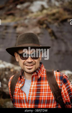 Homme souriant en chapeau et chemise à carreaux dans les montagnes. Banque D'Images