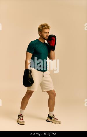 Beau jeune homme se tient dans une posture de boxe, concentré et prêt à s'entraîner dans un studio. Banque D'Images