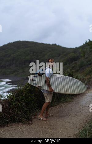 L'homme marche vers la plage avec une planche de surf Banque D'Images