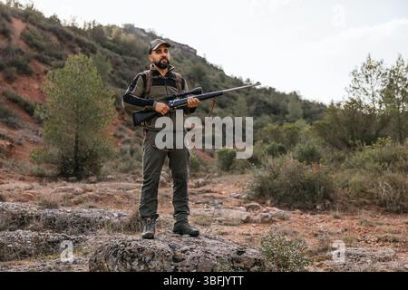 Chasseur debout sur la roche tenant le fusil dans la forêt Banque D'Images