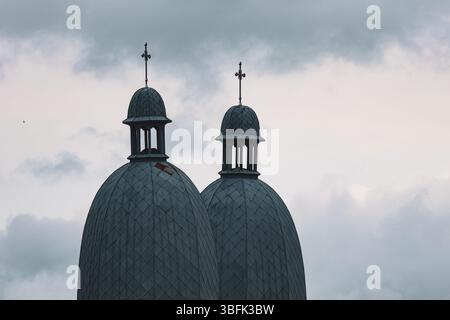 Deux dômes bleus identiques d'une tour d'église silhouettés contre un ciel nuageux de humeur sombre, avec des embouts croisés Banque D'Images