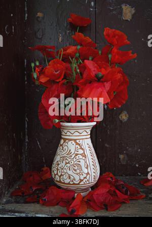 Vase rustique en poterie roumaine regorge de fleurs sauvages et de coquelicots vibrants, mêlant tradition et nature dans un cadre coloré et chaleureux Banque D'Images