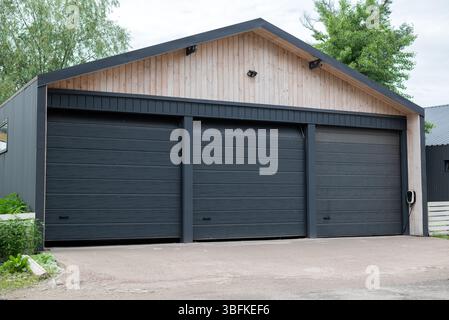 Garage moderne à trois portes avec portails automatiques noirs et façade en bois clair, situé sur une allée en béton propre. Banque D'Images