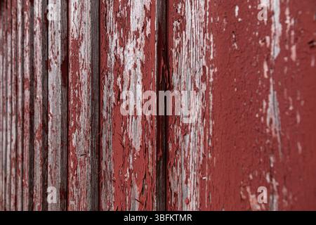 Gros plan d'un mur en bois altéré en Falu Red avec de la peinture écaillée, tourné à un angle pour la profondeur et le flou. Texture de surface rustique nordique. Banque D'Images