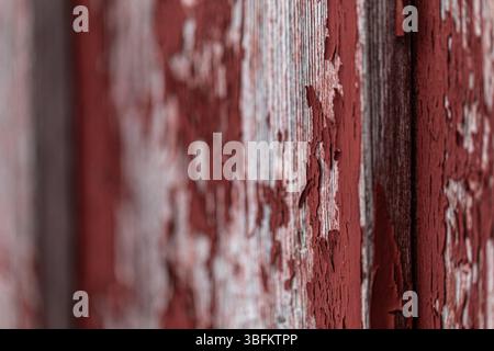 Gros plan d'un mur en bois altéré en Falu Red avec de la peinture écaillée, tourné à un angle pour la profondeur et le flou. Texture de surface rustique nordique. Banque D'Images
