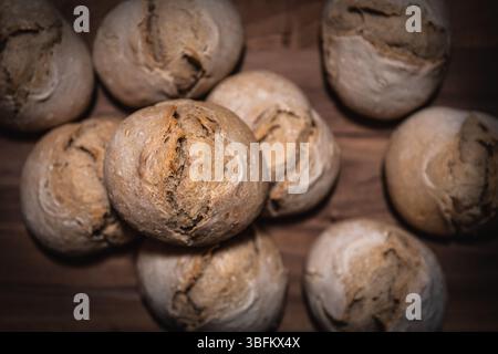 Pile de rouleaux de levain faits maison sur une planche de bois, focus sur le rouleau supérieur, d'autres légèrement floues, prise de vue studio descendante. Banque D'Images